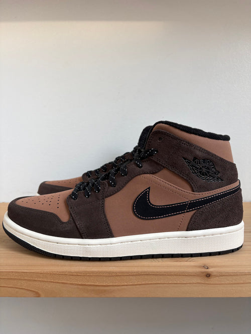 A pair of brown suede and leather high-top sneakers with black accents and a white midsole, displayed on a wooden surface against a plain light background.